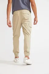 Pantalón cargo color beige con ajuste slim, cintura elástica con cordón ajustable, bolsillos laterales con solapa y velcro, y puños elásticos en los tobillos.