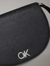 Cartera de hombro tipo saddle de Calvin Klein, color negro, con textura de lino tejido en piel sintética. Presenta correa ajustable, cierre de solapa con broche giratorio y herraje metálico con el monograma CK en la parte delantera.