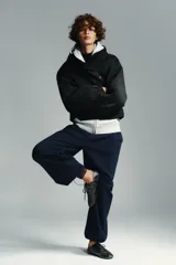 Anorak corto de color negro con acolchado interior, cuello subido y capucha. Presenta mangas largas con puños elásticos, bolsillos delanteros con cierre y bajo ajustable con cordones. Cierre frontal con cremallera termosellada y botones a presión.