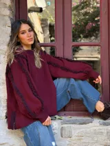 Sweater de punto color bordó con diseño de mangas abullonadas y detalles de flecos en las costuras de los hombros y mangas. Presenta cuello redondo y aberturas laterales en el ruedo.