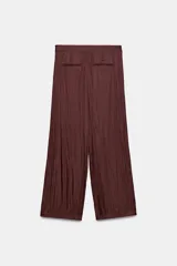 Pantalón de tiro medio con diseño tipo pareo, confeccionado en tejido satinado con acabado arrugado. Presenta pernera recta, cierre frontal con botón a presión y cremallera lateral oculta.