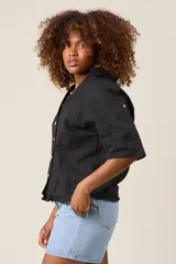 Camisa color beige claro, de corte clásico, con cuello, botones frontales, bolsillo en el pecho y mangas tres cuartos con presilla para sujetar.