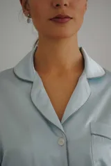 Pijama de satén elastizado color celeste, compuesto por una camisa de manga larga con cuello solapa, botones frontales y bolsillo en el pecho, y un pantalón recto con cintura elástica y lazo ajustable.