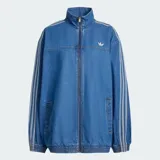 Chaqueta deportiva Adidas Firebird Adilenium de denim, color azul, con cuello alto, cierre frontal y las clásicas tres tiras en las mangas. Cuenta con bolsillos frontales ribeteados y el logo del trifolio bordado en el pecho.