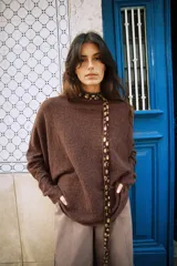 Jersey de punto color marrón con cuello subido y manga larga. Presenta un diseño de cuerpo amplio estilo capa con sisa ancha y bajo asimétrico con aberturas laterales.
