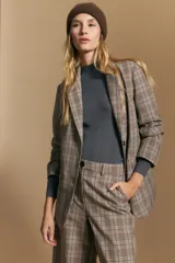 Blazer de corte sastrero con estampado de cuadros en tonos beige, marrones y rojizos. Presenta solapas clásicas, cierre frontal con un botón y bolsillos laterales con solapa.