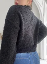 Sweater negro de cuello alto con apliques de flores tejidas en rosa, amarillo y azul.