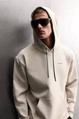 Sudadera de hombre Zara Athleticz de ajuste relajado (relaxed fit), color marrón, confeccionada en tejido técnico compacto con mezcla de algodón y elasticidad. Cuenta con cuello con capucha ajustable con cordones negros, manga larga, bolsillo frontal tipo canguro con un pequeño bolsillo termofijado con cierre, y acabados con rib en puños y cintura.