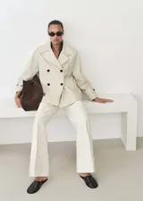 Anorak color beige con cuello de solapa, doble botonadura, manga larga con trabillas y dos bolsillos laterales. Diseño recto y midi con forro interior.