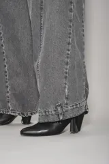 Jean de corte wide leg en color gris oscuro con efecto lavado. Presenta costuras verticales decorativas a lo largo de las piernas y cierre frontal con botón y cremallera.