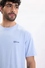 Remera celeste de manga corta, con calce relajado y pequeño estampado tipográfico en el pecho con el texto 'Arrival Coastal Club 1997'.