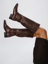 Botas de caña alta color marrón, confeccionadas en cuero con textura lisa y paneles laterales con efecto croco. Cuentan con cierre lateral completo y taco cuadrado bajo.