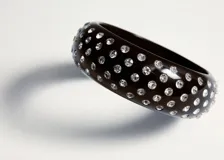 Pulsera rígida de resina color negro, con diseño abovedado y apliques de cristales brillantes distribuidos por toda la superficie.