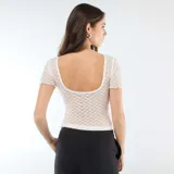 Camiseta de encaje blanco con textura de puntos, cuello redondo y mangas cortas con terminación ondulada.