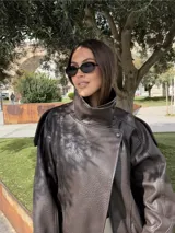 Chaqueta de efecto cuero con cuello alto, cierre frontal cruzado con botones a presión, hombreras y cintura elástica. Presenta un acabado texturizado y bolsillos laterales.