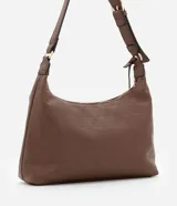 Cartera mediana tipo hobo de Satinato, confeccionada en poliuretano con textura granulada y diseño geométrico sutil. Cuenta con cierre superior de cremallera, correa de hombro ajustable y un dije decorativo metálico con forma triangular.