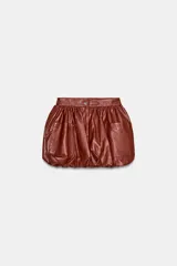Falda mini de estilo globo confeccionada en material con efecto piel color marrón. Presenta diseño abullonado, bolsillos delanteros de plastrón y cierre frontal con cremallera y botón a presión.
