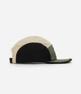 Gorra tipo 5 panel confeccionada en microfibra de poliamida, con diseño de bloques de colores en beige, negro y verde oliva. Presenta visera recta, cierre posterior ajustable y etiqueta frontal con gráfico y frase Stay Grounded.
