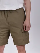 Bermuda de gabardina color verde militar, con cintura elástica ajustable con cordón, bolsillos laterales y bolsillo cargo con solapa en la pierna.