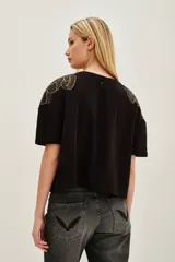 Remera de algodón color negro, de corte holgado y manga corta, con detalle de bordado en forma de plumas en los hombros.