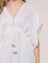 Vestido largo blanco confeccionado en viscosa con hilos de lurex, escote en V profundo con lazo y borlas, mangas kimono y falda fluida con volados en el ruedo.