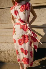 Vestido midi de color beige con estampado floral en tonos rojos y fucsias, con cuello fluido, manga sisa y cinturón del mismo tejido.