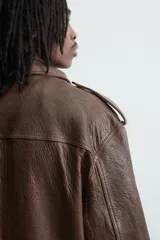 Cazadora biker de corte oversize confeccionada en piel color marrón. Presenta cuello con solapas de pico, cierre frontal asimétrico con cremallera, bolsillos laterales de vivo y bajo con elástico. Las mangas largas cuentan con puños ajustables con cremallera.