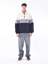 Buzo de tejido polar texturizado, color azul petróleo, con cuello alto y cierre parcial frontal. Presenta un diseño de bloques de color horizontal: blanco crema en la parte superior, gris claro en el medio y azul petróleo en la parte inferior y mangas.