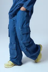 Pantalón tipo cargo de jean azul con corte oversize y tiro medio. Presenta múltiples bolsillos laterales y delanteros con solapa, confeccionado en algodón.
