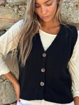 Chaleco tejido de punto color negro, con escote en V y cierre frontal de tres botones grandes de madera. Presenta un diseño clásico y versátil.