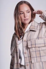 Sobrecamisa de franela color beige con estampado a cuadros en tonos marrones y azules, de corte holgado, con cuello clásico, cierre abotonado y bolsillos delanteros con solapa.