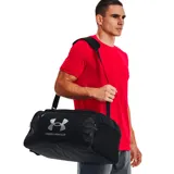 Bolso Under Armour unisex, modelo Undeniable 5.0, color gris con detalles en negro y amarillo. Cuenta con tecnología UA Storm repelente al agua, paneles inferiores y laterales resistentes, bolsillo ventilado para ropa o calzado, bolsillos interiores para organización, bolsillo frontal con cierre, doble bolsillo para botella de agua y correa ajustable para el hombro.
