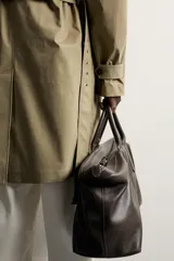 Trench regular fit de color beige, confeccionado en tejido técnico repelente al agua, con diseño de botonadura cruzada, cuello con solapas, mangas raglán con trabillas ajustables en los puños y cinturón del mismo tejido.