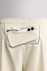Shorts deportivos de entrenamiento Zara Athleticz, color beige, confeccionados en tejido técnico ligero y elástico con forro interior. Presentan cintura elástica ajustable, bolsillos frontales, bolsillo trasero de seguridad con cierre, aberturas laterales en el bajo y detalle de logo estampado en la pierna.