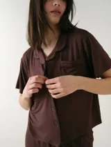 Camisa de manga corta para dormir de color rosado, confeccionada en viscosa. Presenta botones frontales, cuello con solapa, bolsillo en el pecho y ribetes a tono.