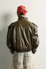 Cazadora cropped fit de color verde militar, confeccionada en tejido efecto piel. Presenta cuello subido, manga larga con puño abotonado, trabillas en los hombros, y bolsillos delanteros de plastrón con solapa. Su diseño incluye bajo elástico y cierre frontal con cremallera oculta por solapa con botones a presión.