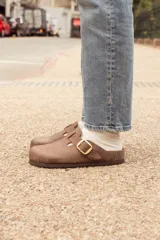 Zueco marrón de cuero con hebilla dorada ajustable.