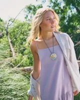 Collar artesanal con dije central de metal con textura orgánica irregular que evoca una ostra. El dije está montado sobre un cordón de algodón natural, permitiendo un uso versátil y regulable.