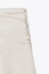 Falda pantalón corta color beige claro, de tiro medio, con efecto drapeado en la cintura y volantes superpuestos en el ruedo.