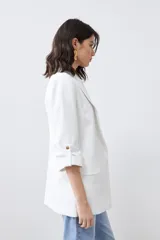 Blazer de corte recto y diseño minimalista, color blanco, con solapas clásicas, bolsillos frontales con solapa y mangas tres cuartos con detalle de botones.
