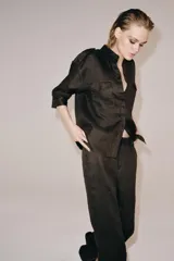 Pantalón flare de tiro medio confeccionado en lino color marrón. Cuenta con cintura con trabillas, bolsillos delanteros, perneras de corte evasé y cierre frontal con cremallera y botón.