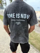 Remera oversize de color celeste melange, con diseño de estampado tipográfico en la espalda que incluye la frase "Time is Now" y otros detalles de colección.