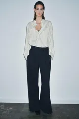 Camisa de corte oversize confeccionada en tejido con viscosa, con estampado de rayas verticales. Presenta cuello mao, cierre frontal con botones ocultos bajo solapa, mangas largas con puños anchos y bolsillos de plastrón en el delantero. El bajo es asimétrico y redondeado.