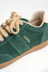 Zapatillas bajas color verde oscuro de gamuza con cordones color beige y suela de goma color marrón.