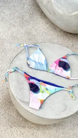 Bikini reversible de diseño triangular con tiras para atar y apliques de argollas metálicas. El conjunto presenta un estampado abstracto multicolor.