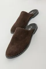 Zuecos de gamuza color marrón chocolate con suela plana y detalle de tachas pequeñas alrededor de la suela.
