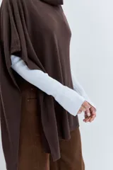 Poncho asimétrico de tejido de punto en color marrón, con cuello alto tipo polera y diseño sin mangas con aberturas laterales.