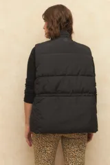 Chaleco puffer color crema, con cuello alto, cierre frontal y cuatro bolsillos con solapa. Cuenta con cintura ajustable con cordón.