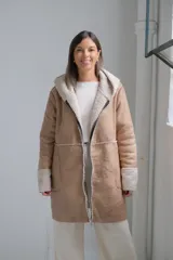 Tapado tipo gamuza con interior de corderito sintético, color beige con detalles en crudo. Presenta capucha, cierre frontal completo y puños con vuelta de corderito.