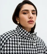 Saco corto estructurado con estampado pied de poule en blanco y negro. Presenta cuello alto, cierre frontal cruzado con botones decorativos y mangas largas.